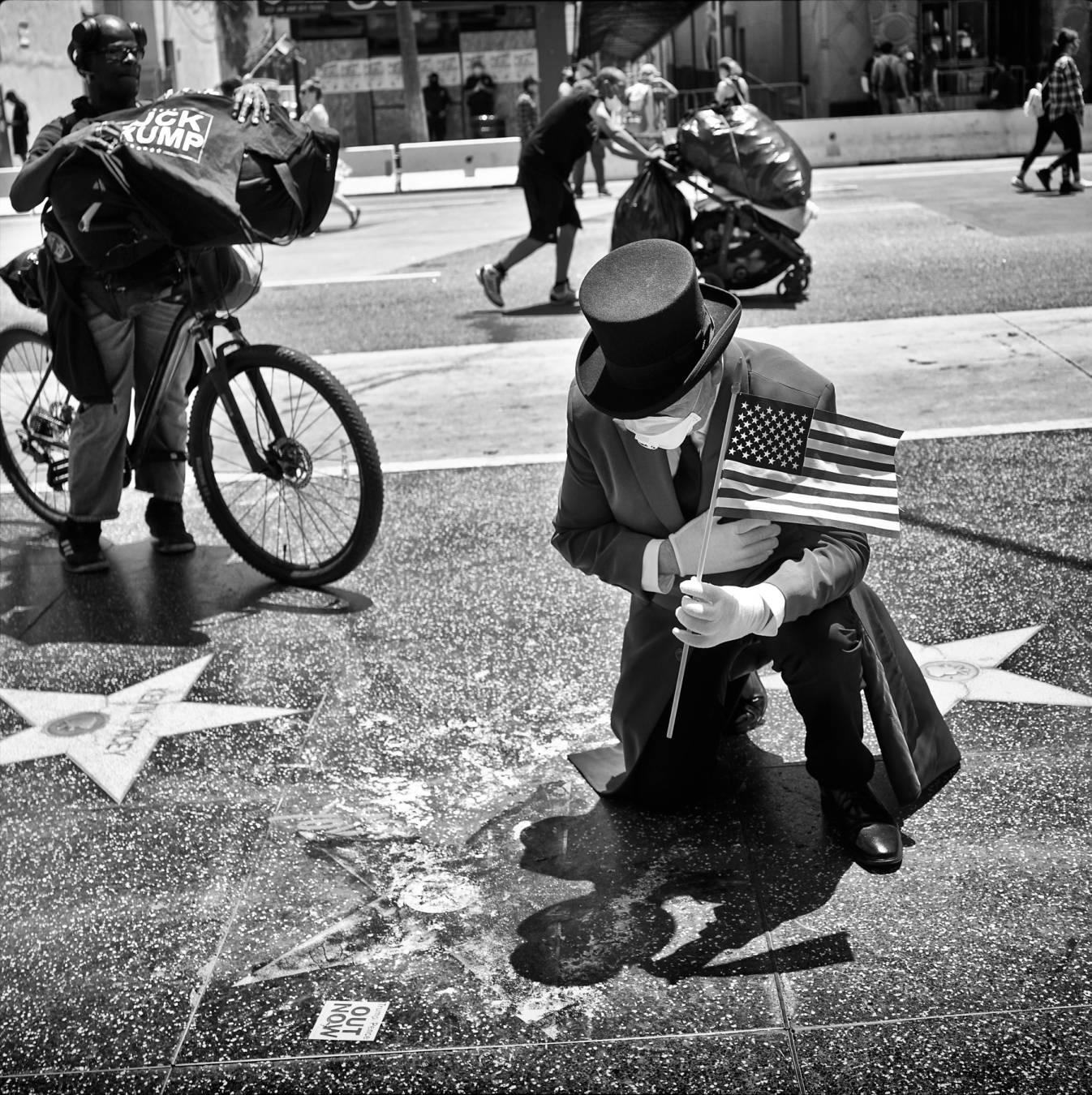 Der ganze Wahnsinn in einem Bild, festgehalten 2020 in Hollywood: Ein Trumpanhänger betet über dessen demoliertem Stern – beobachtet von einem Schwarzen, der eine „Fuck Trump“-Tasche trägt. Im Hintergrund schiebt ein Mann seine Habe auf einem Kinderwagen. Foto: Michael Dressel