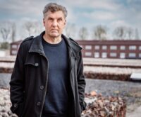 Ein Mann mit grauen Haaren und ernstem Blick steht auf dem Gelände der Gedenkstätte Neuengamme.