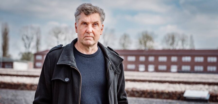 Ein Mann mit grauen Haaren und ernstem Blick steht auf dem Gelände der Gedenkstätte Neuengamme.