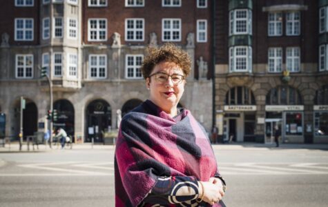 Eine Frau steht vor einem Backsteingebäude und schaut in die Kamera.