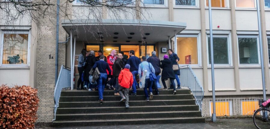 Eine Menschengruppe geht auf die Tür der Unterkunft zu.